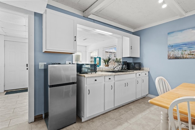 kitchen featuring white cabinets, beam ceiling, sink, and stainless steel refrigerator