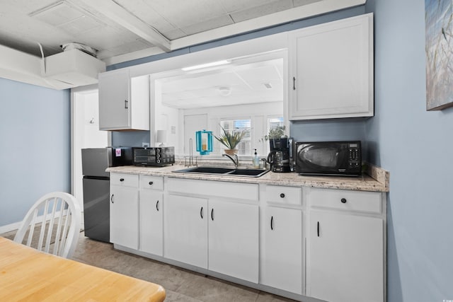 kitchen with white cabinets, refrigerator, sink, beam ceiling, and light stone counters