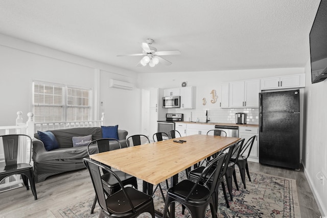 dining space with an AC wall unit, sink, light hardwood / wood-style flooring, ceiling fan, and a textured ceiling