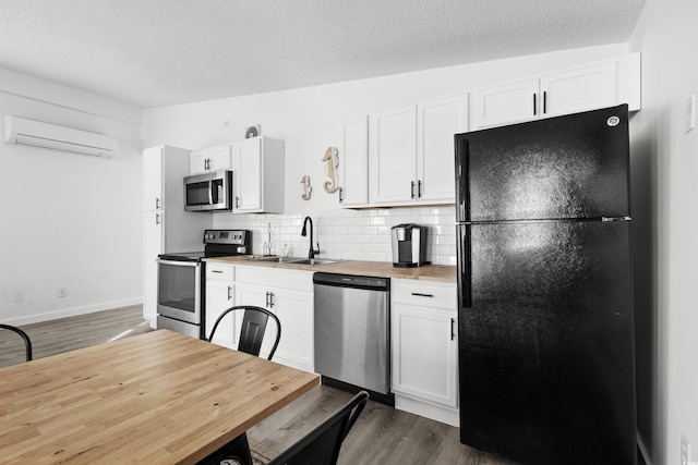 kitchen with white cabinetry, sink, stainless steel appliances, a wall mounted air conditioner, and wooden counters