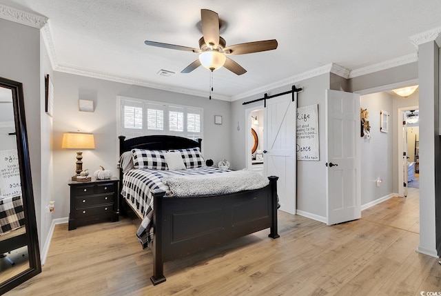 bedroom with a barn door, ceiling fan, crown molding, and light wood-type flooring