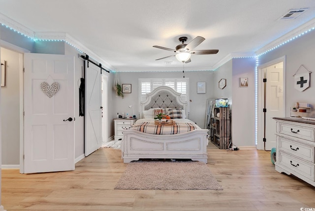 bedroom featuring a barn door, ceiling fan, light hardwood / wood-style flooring, and ornamental molding