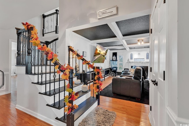 staircase featuring beamed ceiling, wood-type flooring, and coffered ceiling