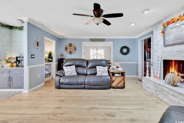 living room featuring ceiling fan, light hardwood / wood-style floors, a stone fireplace, and ornamental molding