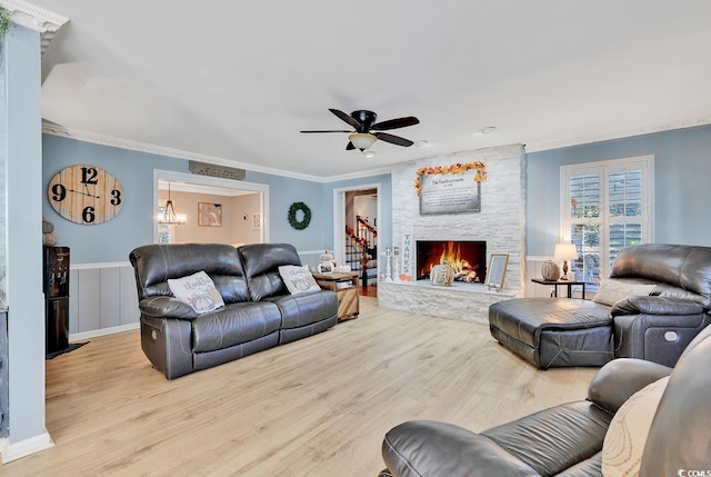 living room with light wood-type flooring, a stone fireplace, ceiling fan, and ornamental molding