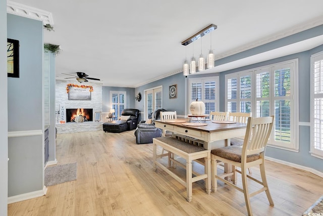 dining room featuring ceiling fan, a fireplace, ornamental molding, and light wood-type flooring