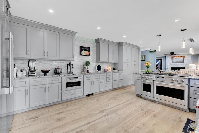 kitchen with double oven range, ceiling fan, decorative backsplash, light wood-type flooring, and light stone counters