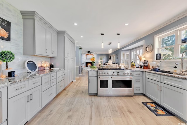 kitchen featuring tasteful backsplash, double oven range, light hardwood / wood-style flooring, a fireplace, and gray cabinets