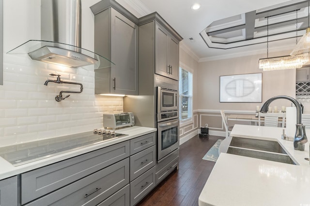 kitchen featuring gray cabinetry, dark wood-type flooring, stainless steel appliances, wall chimney range hood, and tasteful backsplash