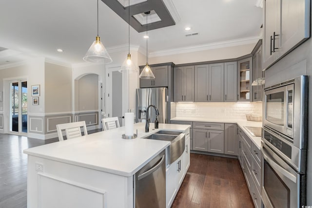 kitchen with appliances with stainless steel finishes, ornamental molding, sink, a center island with sink, and hanging light fixtures