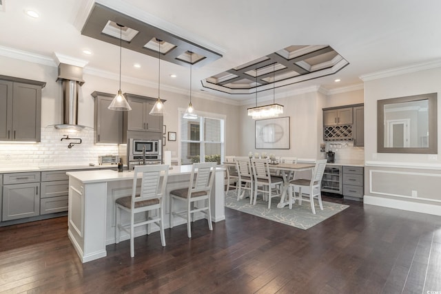 kitchen featuring decorative light fixtures, ornamental molding, an island with sink, and coffered ceiling