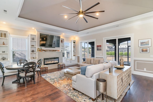 living room featuring ceiling fan, ornamental molding, dark wood-type flooring, and a tray ceiling