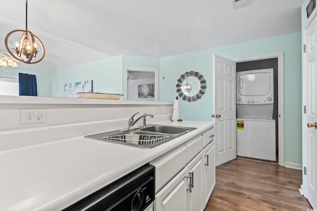 kitchen featuring sink, decorative light fixtures, a notable chandelier, stacked washer and dryer, and white cabinetry