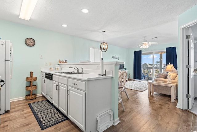 kitchen with dishwashing machine, sink, light hardwood / wood-style flooring, white cabinetry, and hanging light fixtures