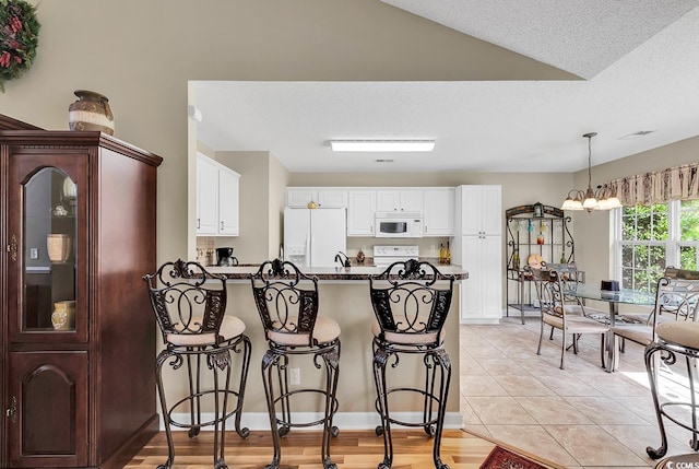 kitchen with kitchen peninsula, white appliances, a notable chandelier, white cabinetry, and light tile patterned flooring