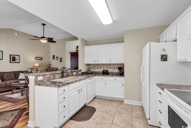 kitchen with white appliances, kitchen peninsula, sink, light tile patterned floors, and white cabinetry