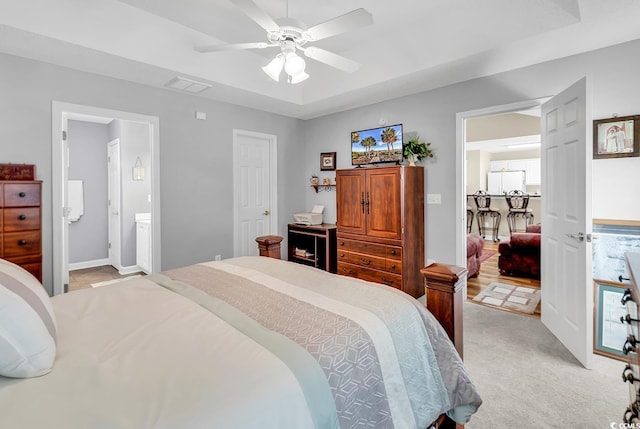 carpeted bedroom featuring ensuite bathroom, ceiling fan, white fridge, and a tray ceiling