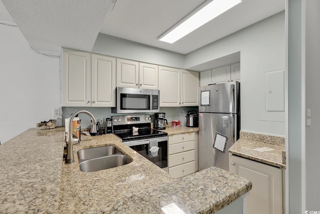 kitchen with white cabinets, sink, appliances with stainless steel finishes, light stone counters, and kitchen peninsula