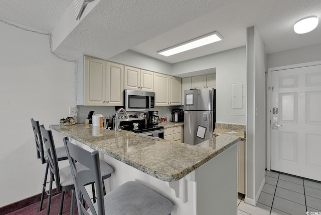 kitchen featuring kitchen peninsula, appliances with stainless steel finishes, a breakfast bar, and a textured ceiling