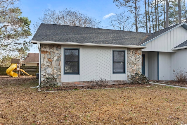 view of side of property featuring a shingled roof, stone siding, a playground, and a yard