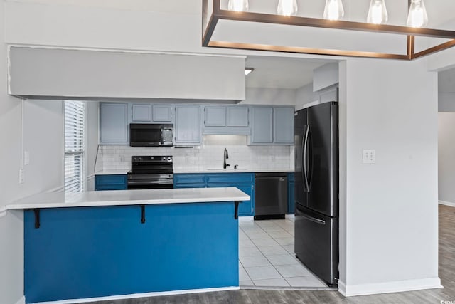 kitchen featuring blue cabinetry, light countertops, backsplash, a peninsula, and black appliances