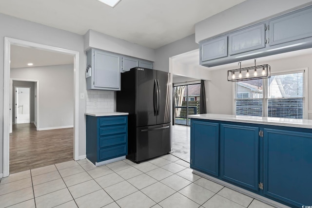 kitchen with blue cabinetry, tasteful backsplash, light countertops, and freestanding refrigerator