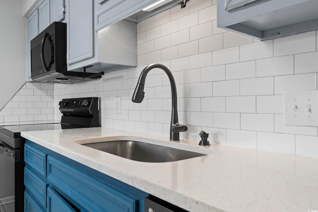 kitchen with light stone counters, blue cabinetry, decorative backsplash, a sink, and black appliances