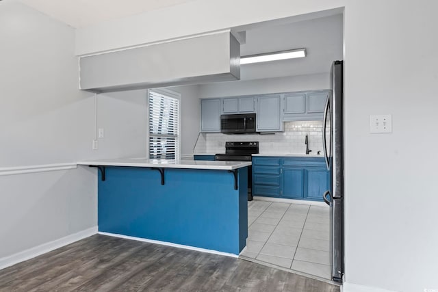 kitchen featuring light countertops, decorative backsplash, appliances with stainless steel finishes, a peninsula, and a kitchen breakfast bar