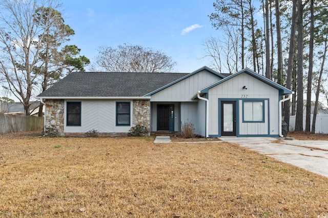 single story home featuring stone siding, a shingled roof, fence, and a front lawn