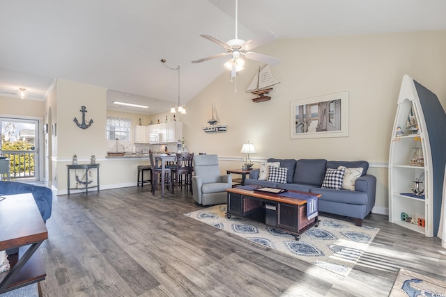 living room with plenty of natural light, ceiling fan with notable chandelier, dark wood-type flooring, and vaulted ceiling