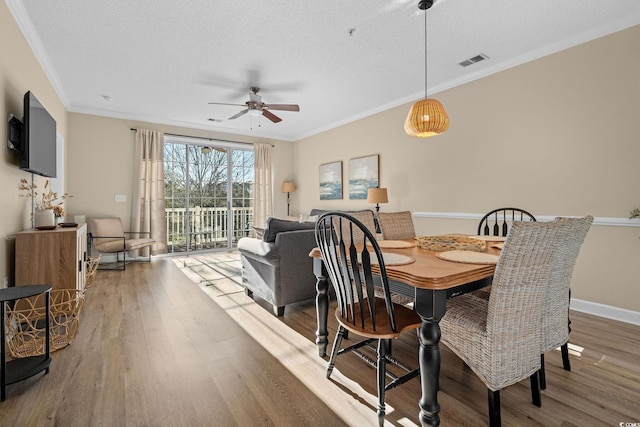 dining space with wood-type flooring, a textured ceiling, ceiling fan, and crown molding