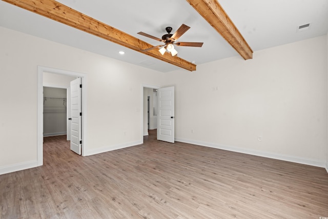 interior space featuring beam ceiling, a walk in closet, light hardwood / wood-style floors, and ceiling fan