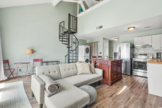 living room featuring beamed ceiling, light hardwood / wood-style floors, high vaulted ceiling, and stacked washer and clothes dryer