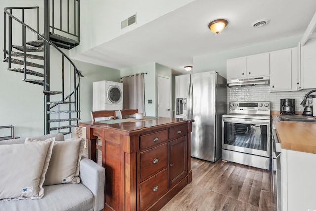 kitchen with appliances with stainless steel finishes, stacked washing maching and dryer, sink, wood-type flooring, and white cabinetry