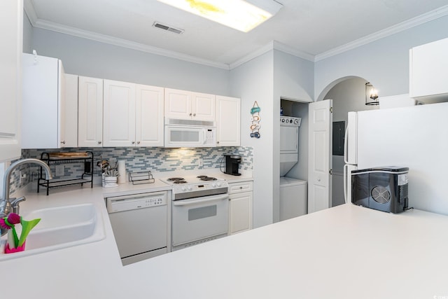 kitchen featuring decorative backsplash, white appliances, sink, stacked washer / dryer, and white cabinetry