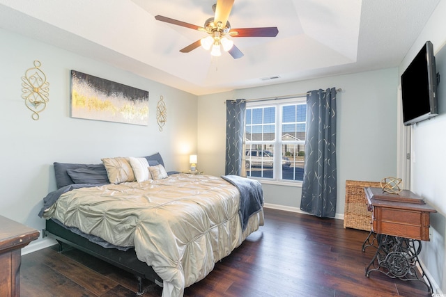 bedroom featuring a raised ceiling, dark wood-type flooring, and ceiling fan