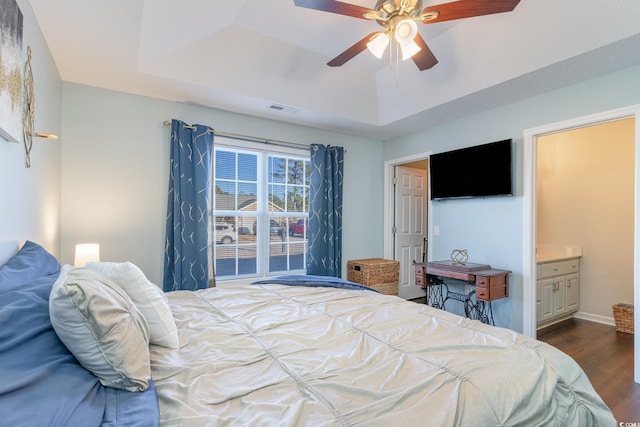 bedroom with dark hardwood / wood-style flooring, ensuite bathroom, ceiling fan, and a tray ceiling