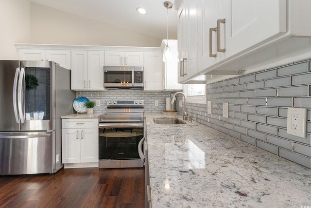 kitchen featuring pendant lighting, sink, appliances with stainless steel finishes, white cabinetry, and vaulted ceiling