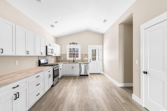 kitchen with sink, stainless steel appliances, backsplash, vaulted ceiling, and white cabinets