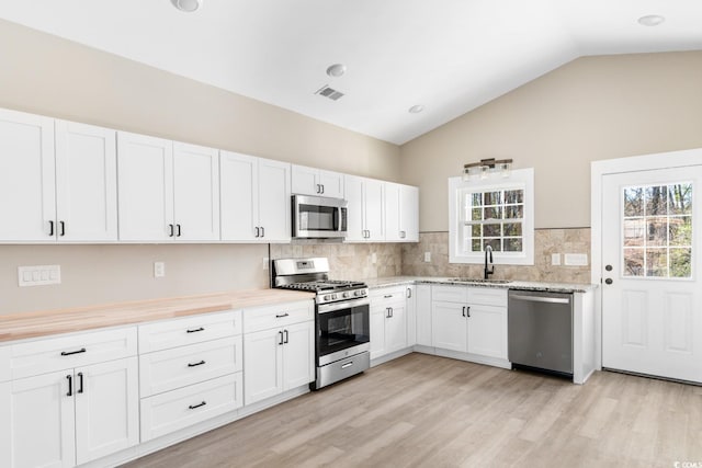 kitchen with lofted ceiling, white cabinets, sink, decorative backsplash, and appliances with stainless steel finishes