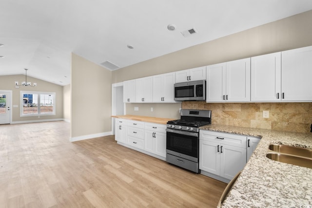 kitchen with sink, stainless steel appliances, an inviting chandelier, lofted ceiling, and white cabinets