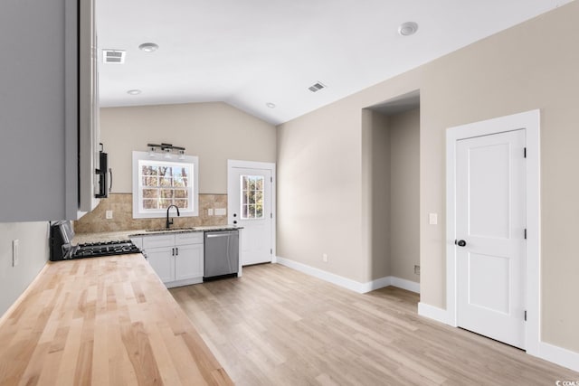 kitchen featuring white cabinetry, sink, stainless steel dishwasher, butcher block countertops, and lofted ceiling