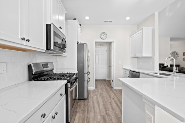 kitchen with sink, light wood-type flooring, light stone counters, white cabinetry, and stainless steel appliances