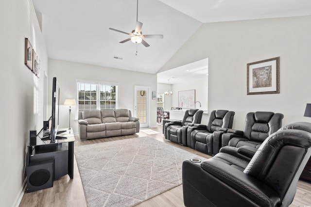 living room with ceiling fan with notable chandelier, high vaulted ceiling, and light hardwood / wood-style flooring