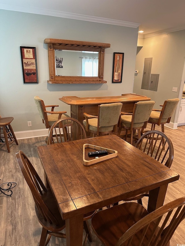 dining area featuring wood finished floors, baseboards, ornamental molding, electric panel, and a bar
