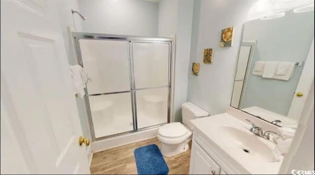 bathroom with wood finished floors, a stall shower, vanity, and toilet