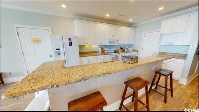 kitchen featuring a kitchen island with sink, white appliances, a breakfast bar, a sink, and white cabinets