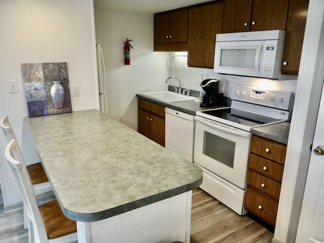 kitchen with sink, kitchen peninsula, light hardwood / wood-style floors, white appliances, and a breakfast bar