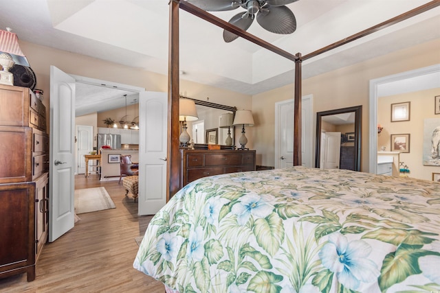 bedroom with lofted ceiling, light wood-type flooring, stainless steel refrigerator, a raised ceiling, and ceiling fan