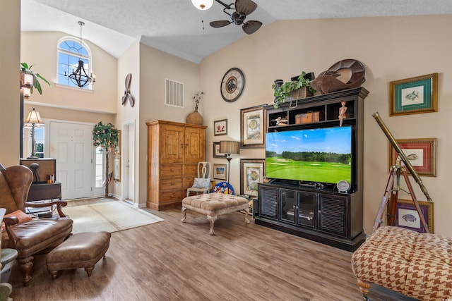 living room featuring ceiling fan with notable chandelier, high vaulted ceiling, hardwood / wood-style floors, and a textured ceiling